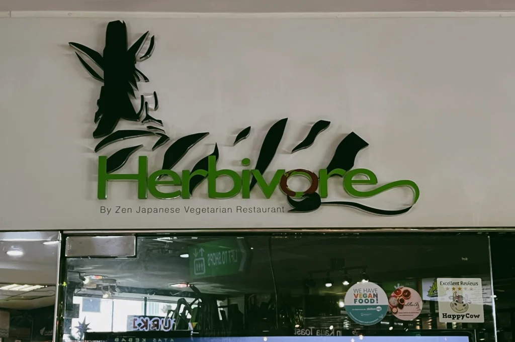 Close-up eye-level shot of Herbivore vegan Japanese restaurant signage at Fortune Centre, known for plant-based sushi and udon dishes
