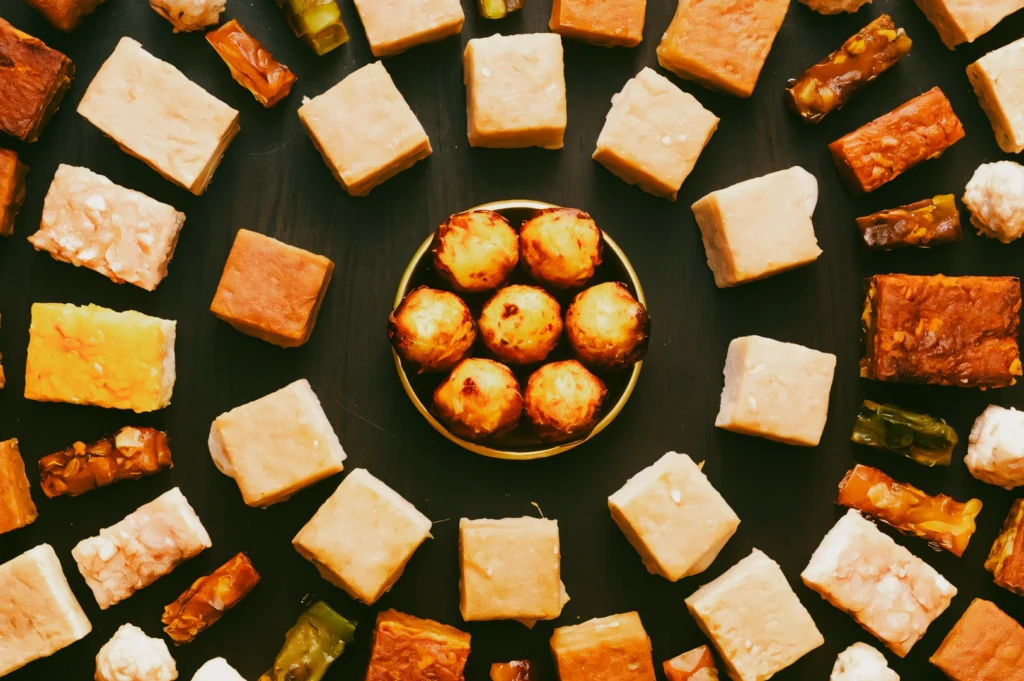 Top-down flat lay shot of assorted vibrant Nonya kueh arranged symmetrically on a dark background, showcasing colorful Peranakan desserts and traditional Singapore heritage food culture