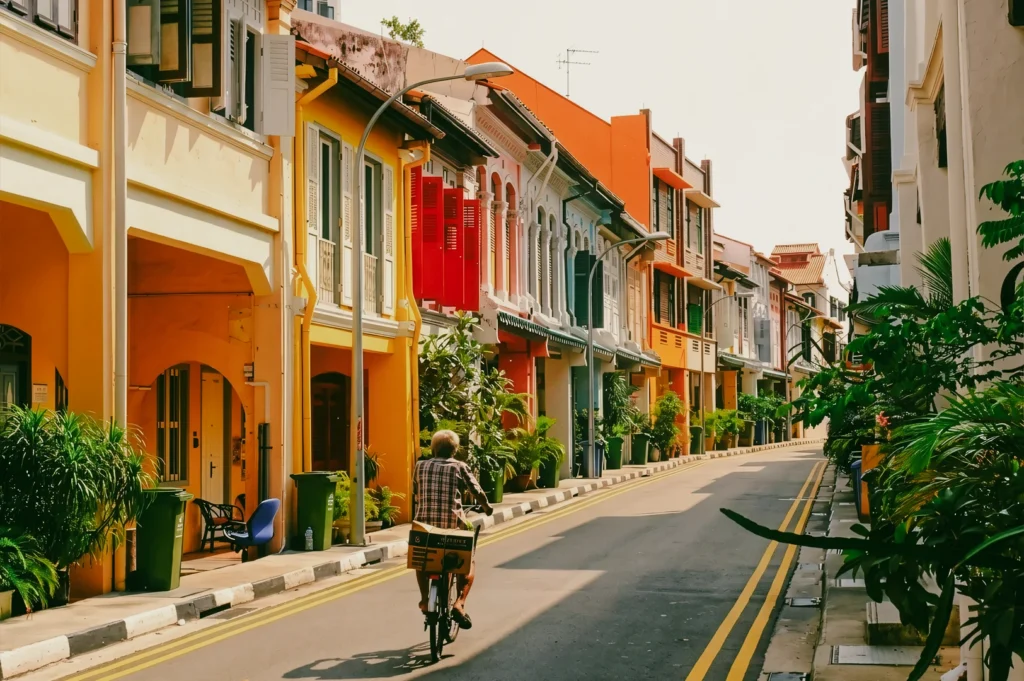 Rear-facing eye-level shot of a cyclist moving through a colourful Singapore neighbourhood street lined with heritage shophouses