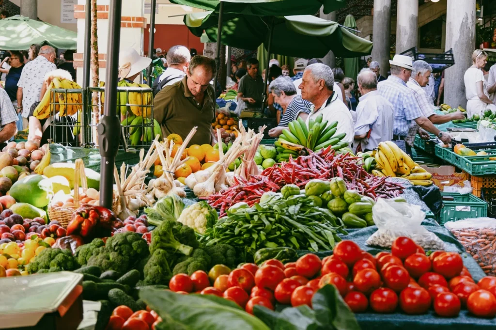 Wide-angle elevated view of a crowded open-air farmers market with colorful fresh produce, illustrating vibrant community interaction, local vendors, and weekend market atmosphere