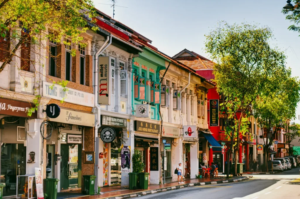 Street-level perspective of Joo Chiat shophouses with local businesses, leafy trees, and vibrant heritage architecture, capturing everyday life in Singapore’s Peranakan cultural neighborhood.