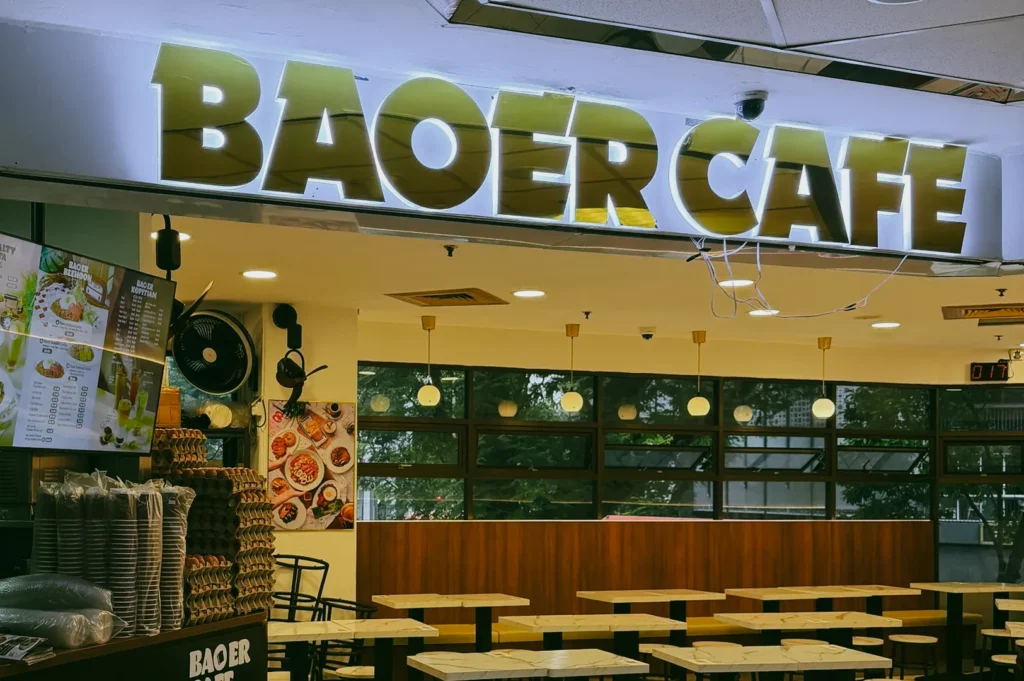 Eye-level wide interior shot of Bao Er Cafe at Fortune Centre, showing casual seating and breakfast items like kaya toast and coffee