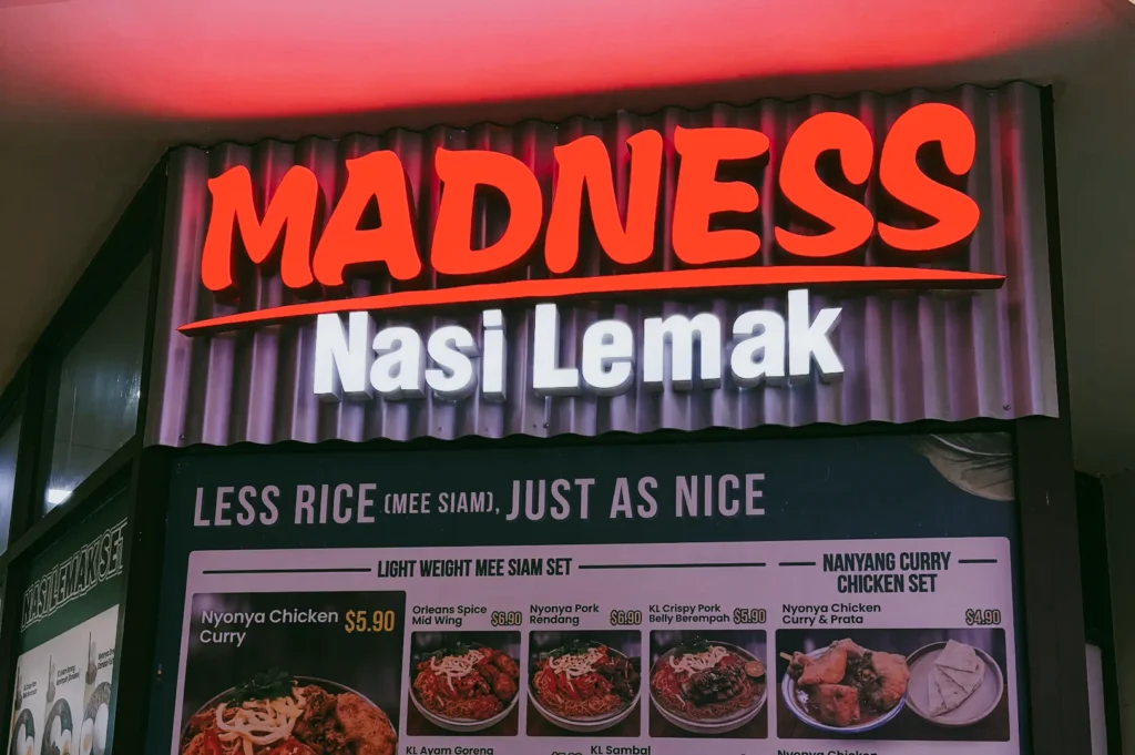 Upward angled close shot of Madness Nasi Lemak signboard at Fortune Centre, featuring popular Singapore nasi lemak stall menu