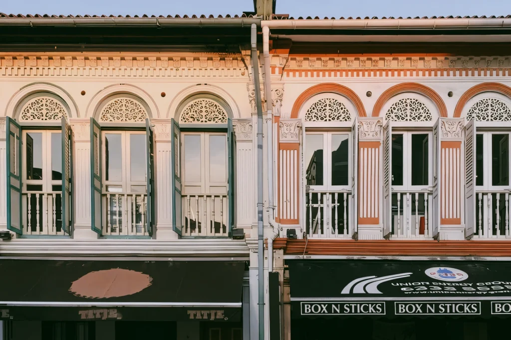 Front-facing symmetrical shot of colorful historic shophouse facades with arched windows and decorative plasterwork, showcasing conserved Singapore heritage streetscape