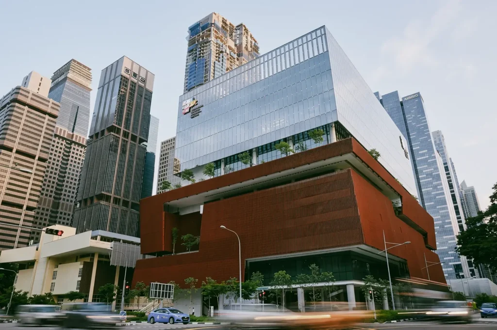 Low-angle architectural shot of Singapore Chinese Cultural Centre building surrounded by modern skyscrapers and city traffic, highlighting contemporary spaces preserving Chinese heritage in Singapore