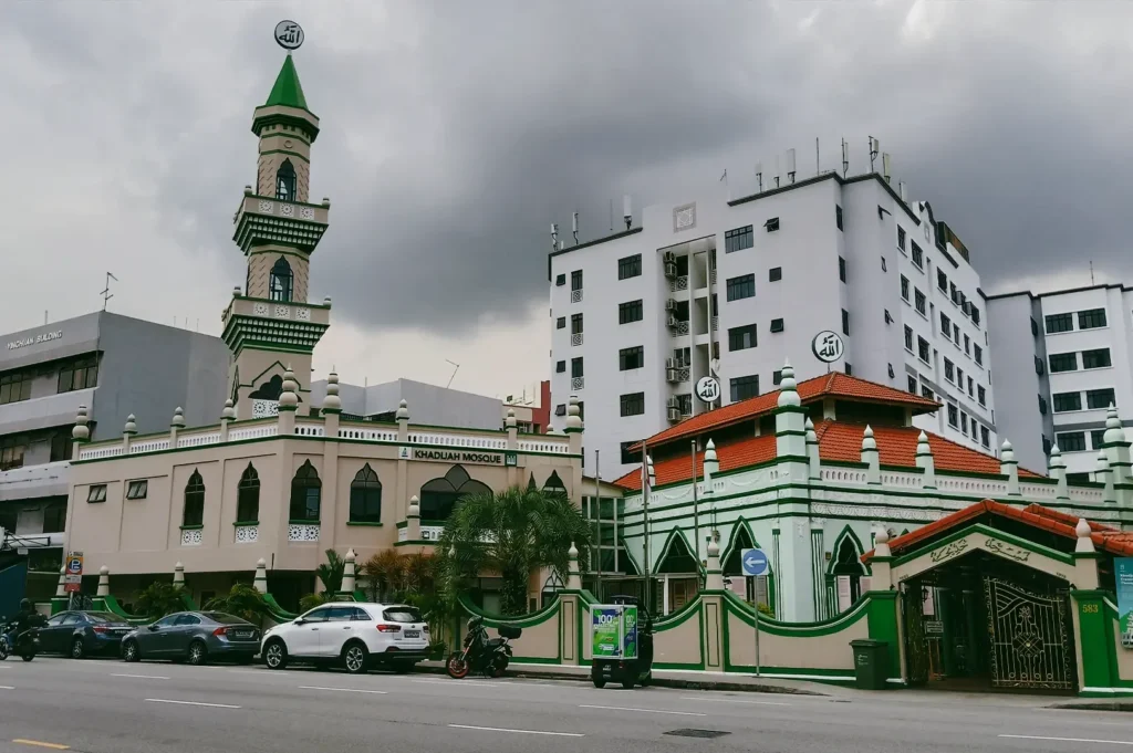 Eye-level wide-angle street shot of Masjid Khadijah along Geylang Road in Singapore, showing the mosque’s green-and-white façade beside modern buildings, illustrating religious diversity in the Geylang neighbourhood.