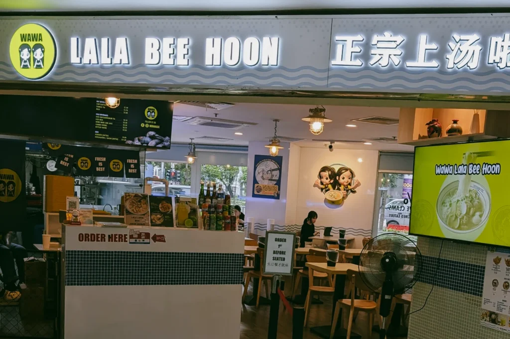 Eye-level wide shot of Wawa Lala Bee Hoon seafood stall at Fortune Centre, showing interior dining area and clam noodle offerings
