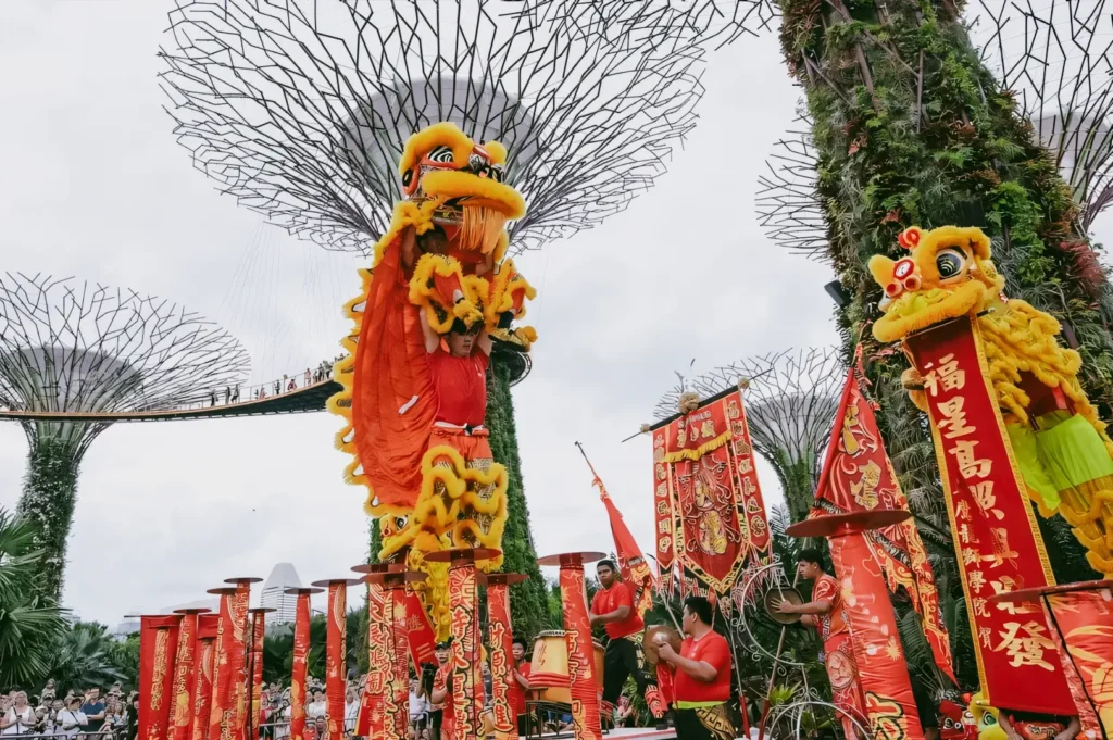 Low-angle wide shot of vibrant Chinese lion dance performance at Gardens by the Bay Singapore with Supertree Grove in background, showcasing traditional festival culture in a modern urban landscape