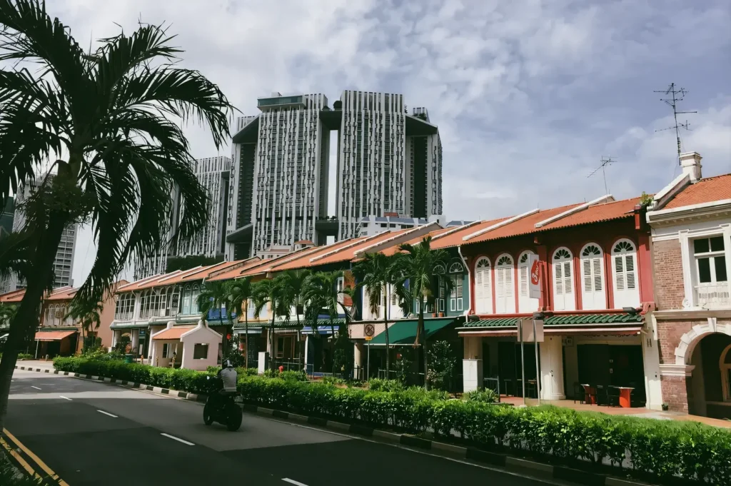 Wide street-level shot of colorful heritage shophouses along Tanjong Pagar Road with modern skyscrapers rising behind, showcasing the contrast between old-world architecture and Singapore’s central business district