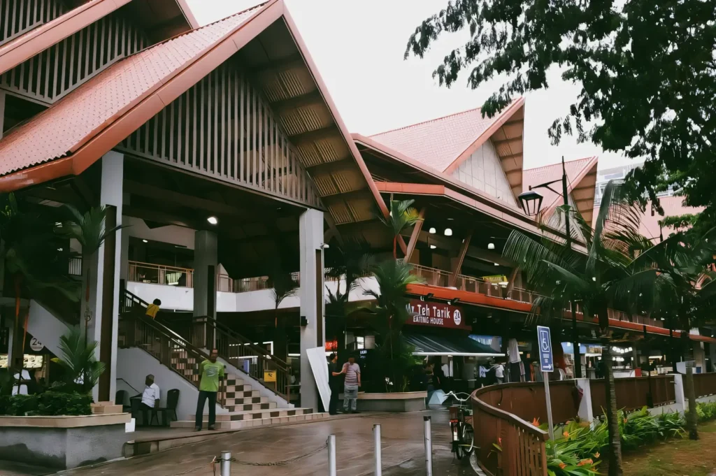 Eye-level wide-angle shot of Geylang Serai Market building in Singapore, featuring traditional Malay-inspired architecture, people entering the market, and lush greenery, highlighting the cultural heart of the Geylang neighbourhood.