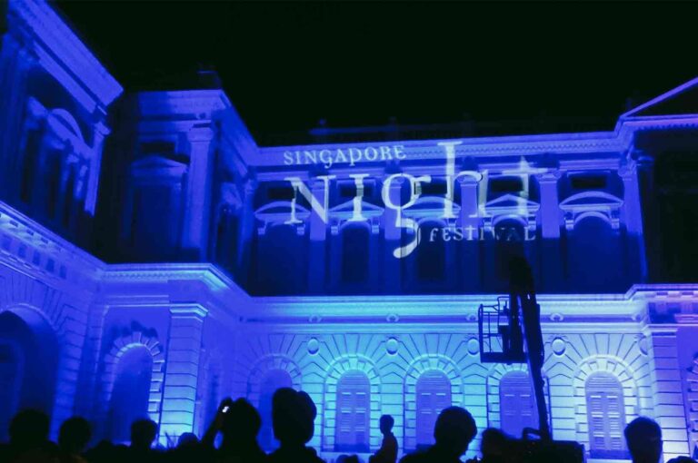 Low-angle wide shot of a colonial-era building illuminated in blue light during the Singapore Night Festival, showcasing cultural activity Singapore through light, art, and architecture.