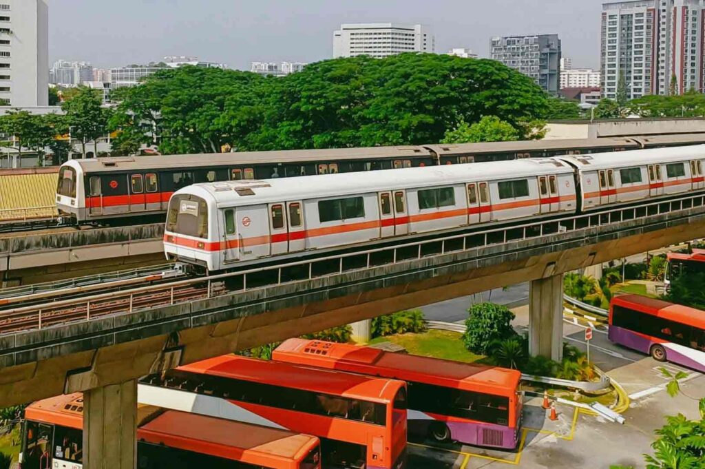 Side-angle wide shot of a Singapore MRT train traveling on an elevated track above buses and greenery, illustrating efficient public transport connecting cultural districts.