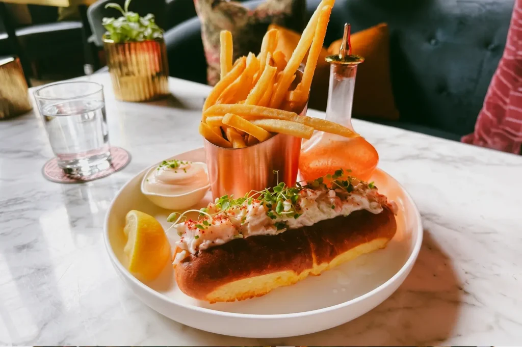 Close-up eye-level shot of ATLAS Bar lobster roll with shoestring fries, lemon wedge and aioli on marble table in Bugis Singapore luxury gin bar