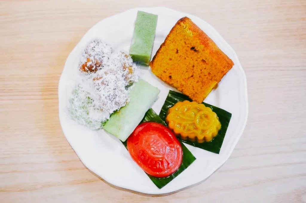 Overhead flat lay of colorful Peranakan kueh assortment including ang ku kueh, ondeh ondeh, and pandan cakes on banana leaves