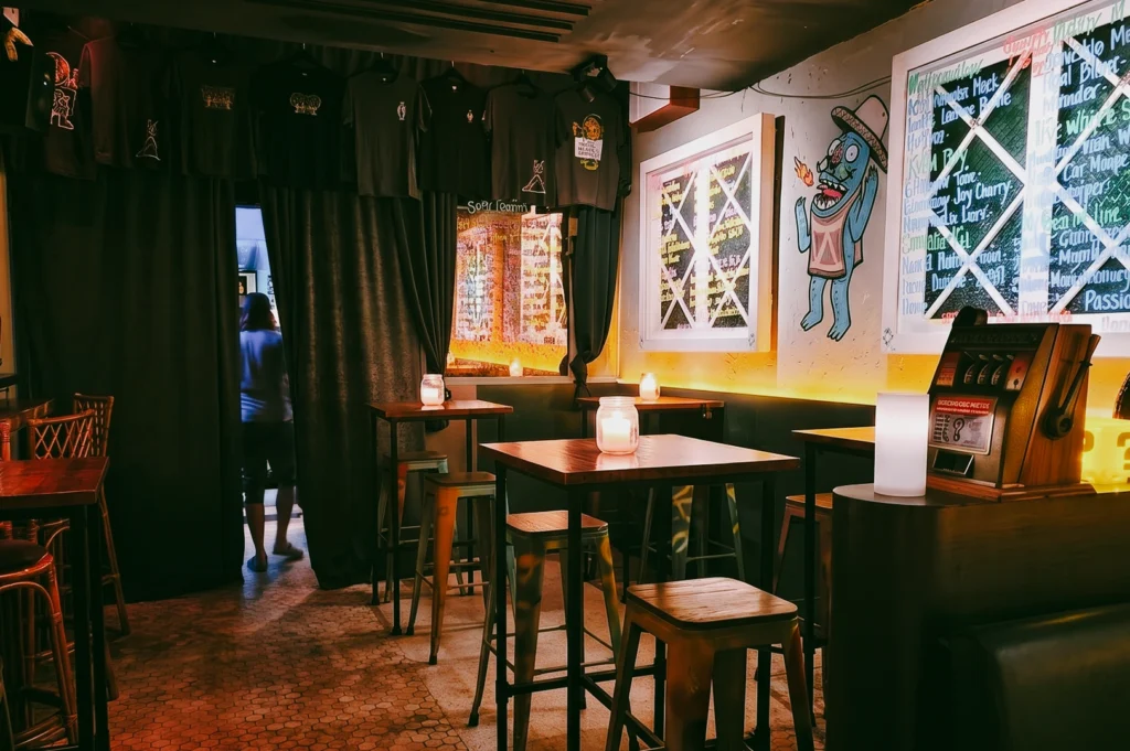 Eye-level wide-angle shot of Sago House Duxton Hill interior showing cosy candlelit tables, salvaged-chic decor, wall art, and intimate seating in a small cocktail bar in Singapore