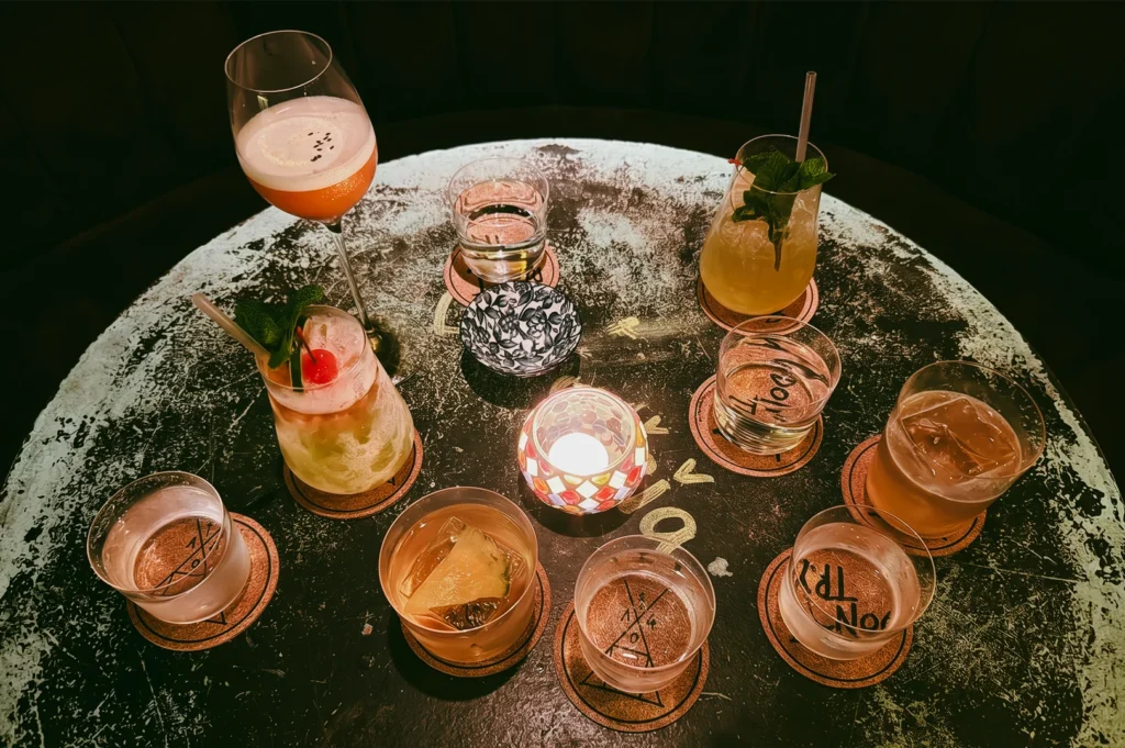 Top-down overhead shot of Sago House rotating cocktails on a round table, featuring creative drinks, whiskey tumblers, citrus garnishes, and candlelight in an intimate Singapore cocktail bar