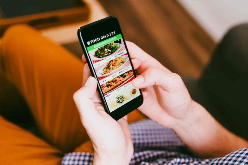 Close-up handheld shot of a smartphone displaying a food delivery app with menu options, illustrating digital convenience, online food ordering, and reduced real-world interaction in modern urban life