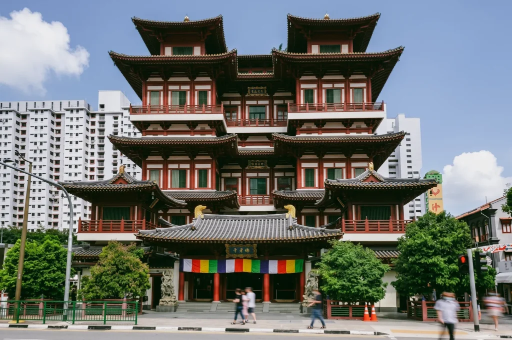 Eye-level symmetrical wide shot of Buddha Tooth Relic Temple in Chinatown Singapore, featuring traditional Tang Dynasty architecture with tiered roofs and modern city buildings in the background.