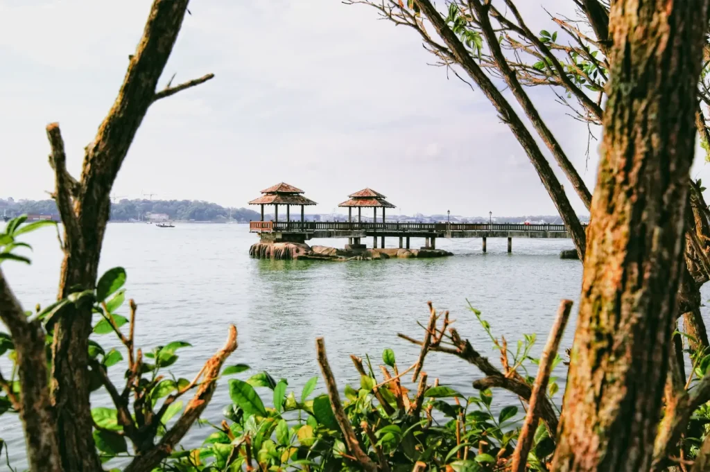 Framed eye-level shot of Pulau Ubin coastline Singapore featuring wooden jetty pavilion over the sea, rustic landscape, and natural coastal greenery, highlighting heritage, nature escape, and island recreation.