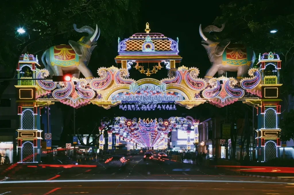 Wide-angle eye-level night shot of Deepavali street light decorations with illuminated elephant arch along Serangoon Road in Little India Singapore, showcasing vibrant Indian festival culture and community celebration