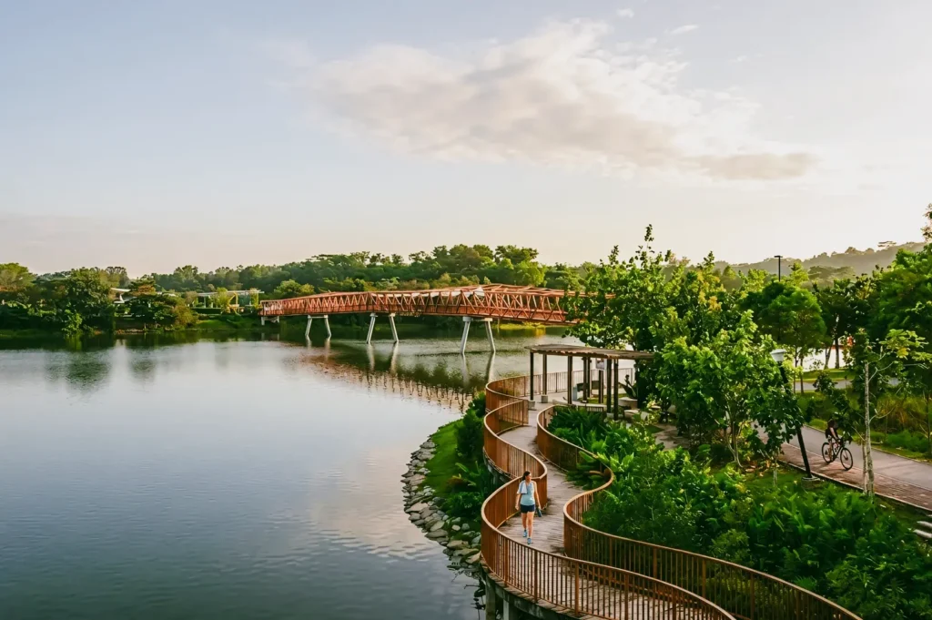 Elevated wide-angle shot of Punggol Waterway Park Singapore featuring a curved waterfront boardwalk, scenic waterway, pedestrian paths, and a signature red bridge, highlighting connected green spaces and active urban lifestyles.
