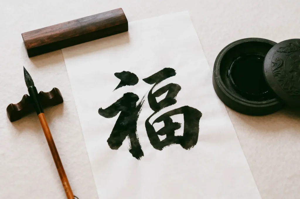 Top-down flat lay shot angle of Chinese calligraphy brush, ink, and paper featuring a bold character, highlighting traditional writing art, cultural heritage, and mindful practice.