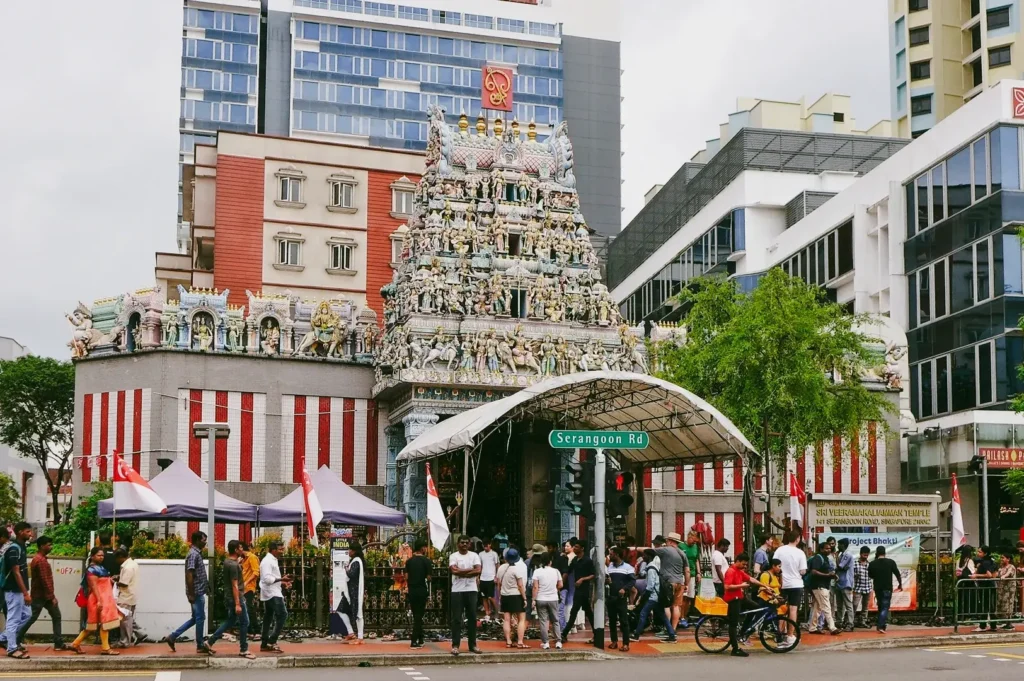 Eye-level wide-angle street view of Sri Veeramakaliamman Temple on Serangoon Road with visitors gathered outside, highlighting Hindu temple architecture and community life in Little India Singapore