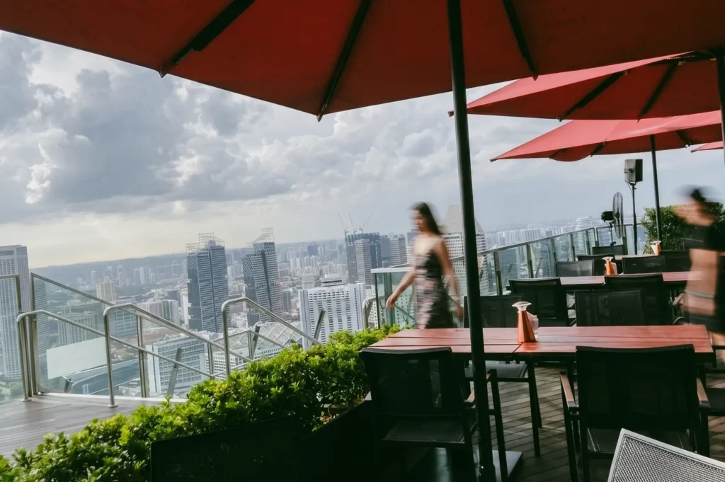 Wide-angle view of rooftop restaurant Singapore at CÉ LA VI featuring terrace seating, red umbrellas, and city skyline backdrop