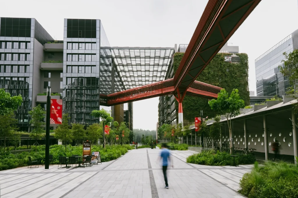 Low eye-level architectural view of Punggol Digital District at Singapore Institute of Technology campus, with modern green buildings, elevated pedestrian bridge, and landscaped walkways, illustrating smart city innovation and sustainable urban development