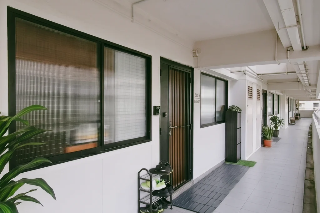 Leading lines corridor perspective shot of a Singapore HDB shared walkway with doors, shoes, and potted plants, highlighting everyday neighbour encounters and communal residential design.