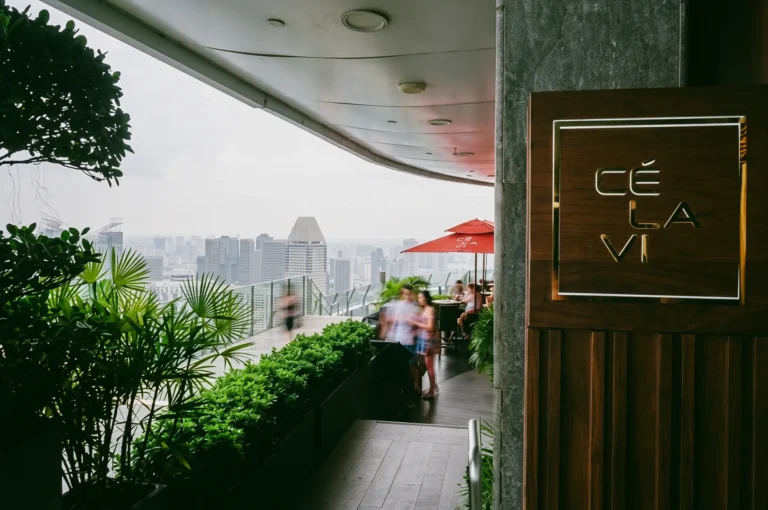 Eye-level wide-angle shot of CÉ LA VI rooftop terrace at Marina Bay Sands, with lush greenery and Singapore skyline views in the background